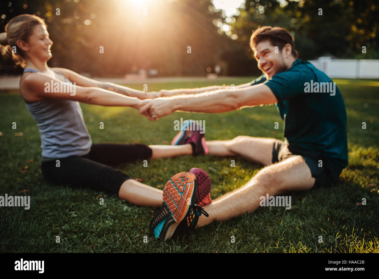 Santé jeune couple doing stretching exercice et réchauffer en parc. L'homme et la femme assis tenant la main et de l'exercice. Banque D'Images