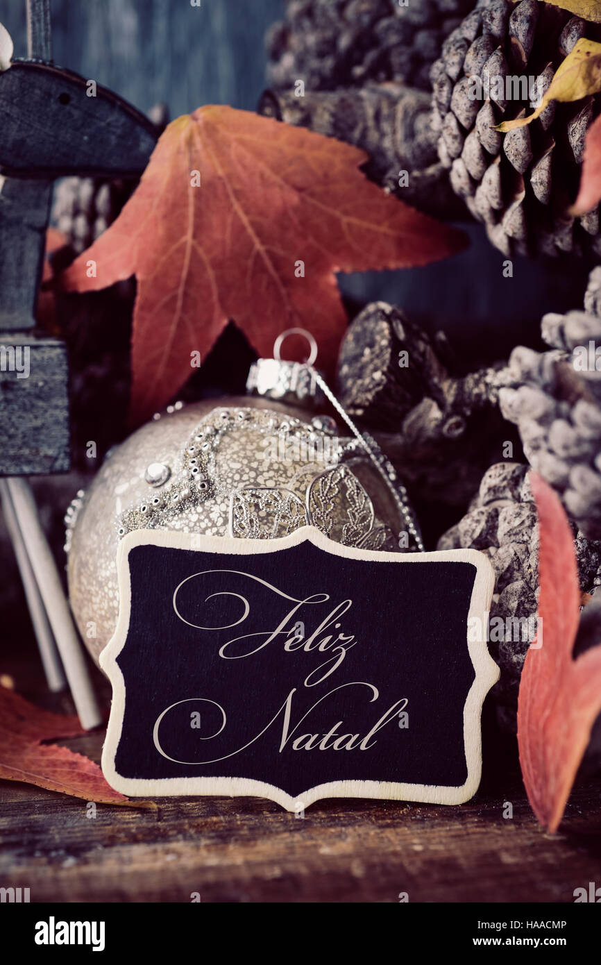Le Texte Feliz Natal Joyeux Noel En Portugais Dans Une Pancarte Noire Placee A Cote D Une Boule De Noel Et Certains Et Certaines Des Feuilles Seches Et De Pin Photo Stock