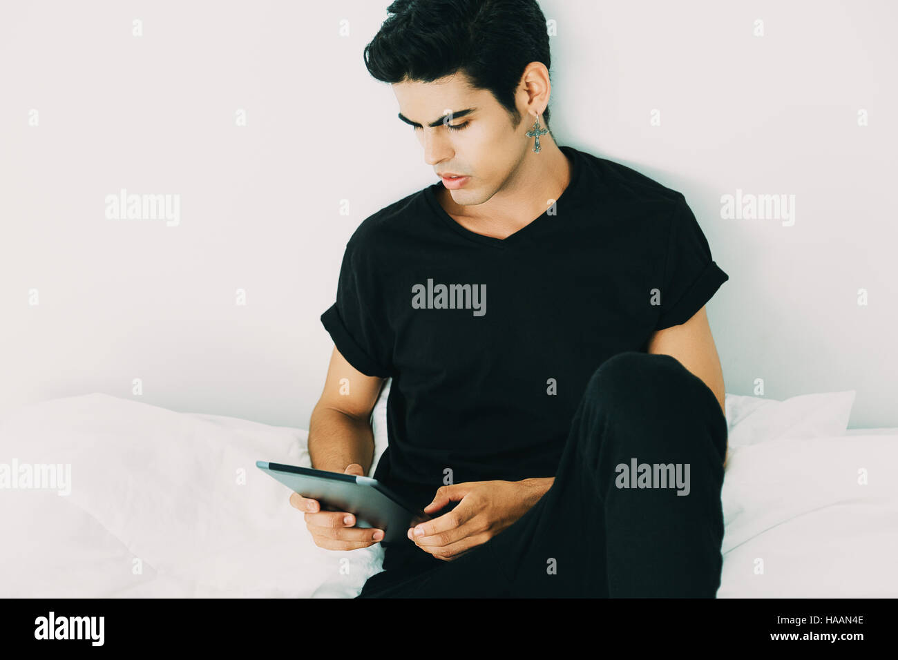 Attrayant beau mec brésilien avec contre-earring en t-shirt noir et des  collants est assis sur le lit et using digital tablet in le matin après le  sommeil Photo Stock - Alamy