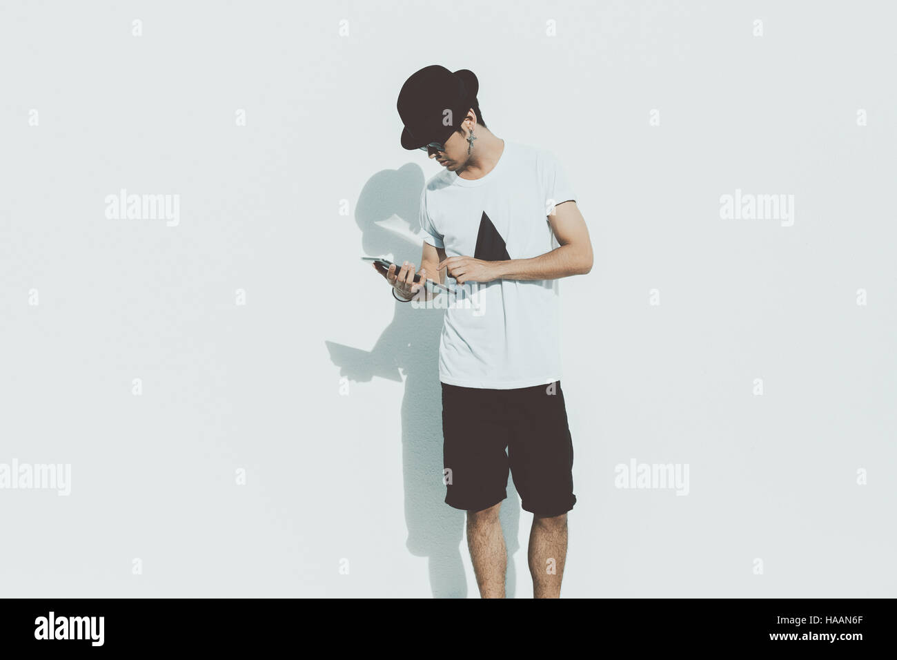 Sérieux attrayant beau jeune mec brésilien moderne dans les lunettes de  soleil, t-shirt blanc, short black hat et travaillant sur tablette  numérique Photo Stock - Alamy