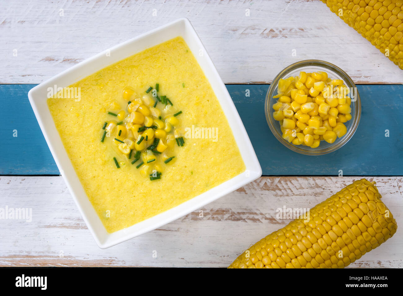 Soupe de maïs dans un bol blanc sur bleu et blanc fond de bois Banque D'Images