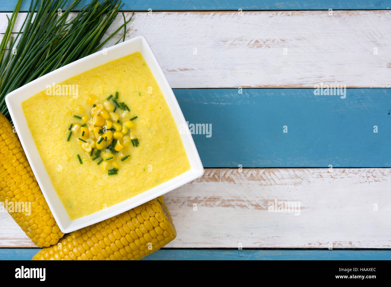 Soupe de maïs dans un bol blanc sur bleu et blanc fond de bois Banque D'Images