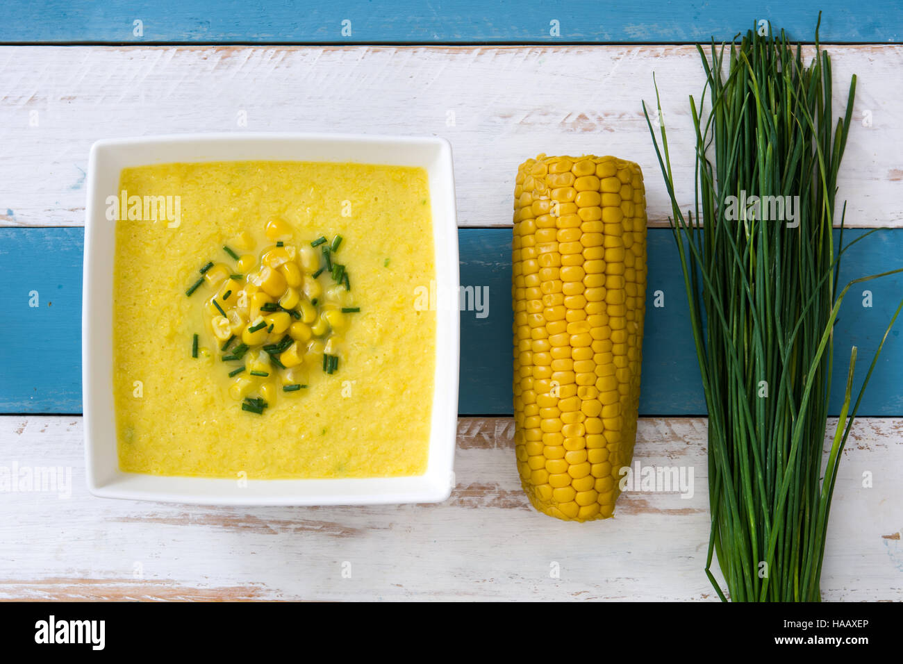 Soupe de maïs dans un bol blanc sur bleu et blanc fond de bois Banque D'Images