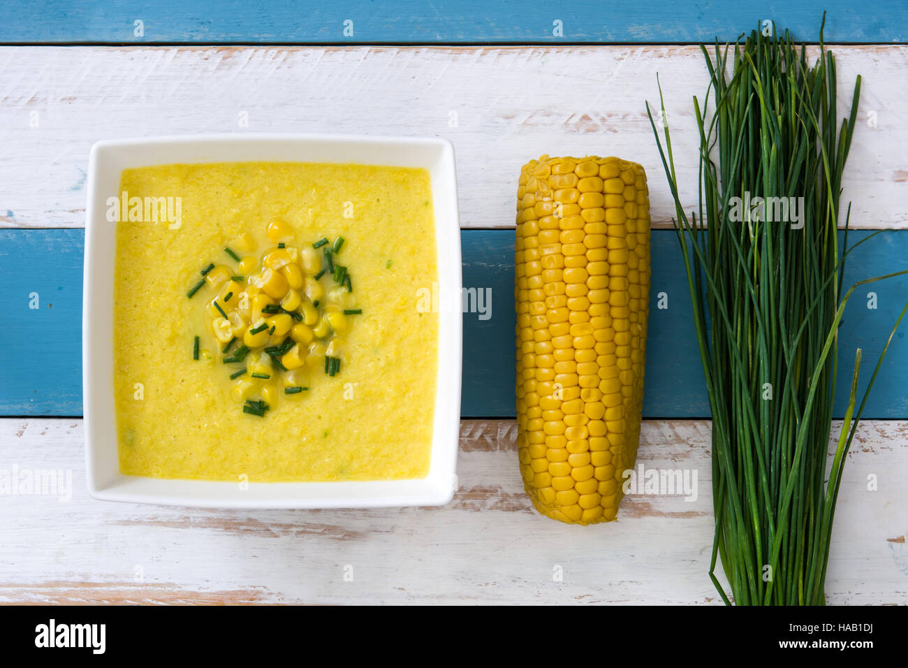 Soupe de maïs dans un bol blanc sur bleu et blanc fond de bois Banque D'Images