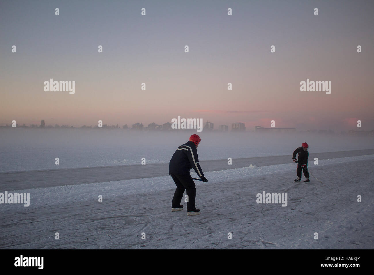 Père et fils de hockey sur glace de la formation d'un lac gelé avec une ville de brouillard à l'arrière-plan. Banque D'Images