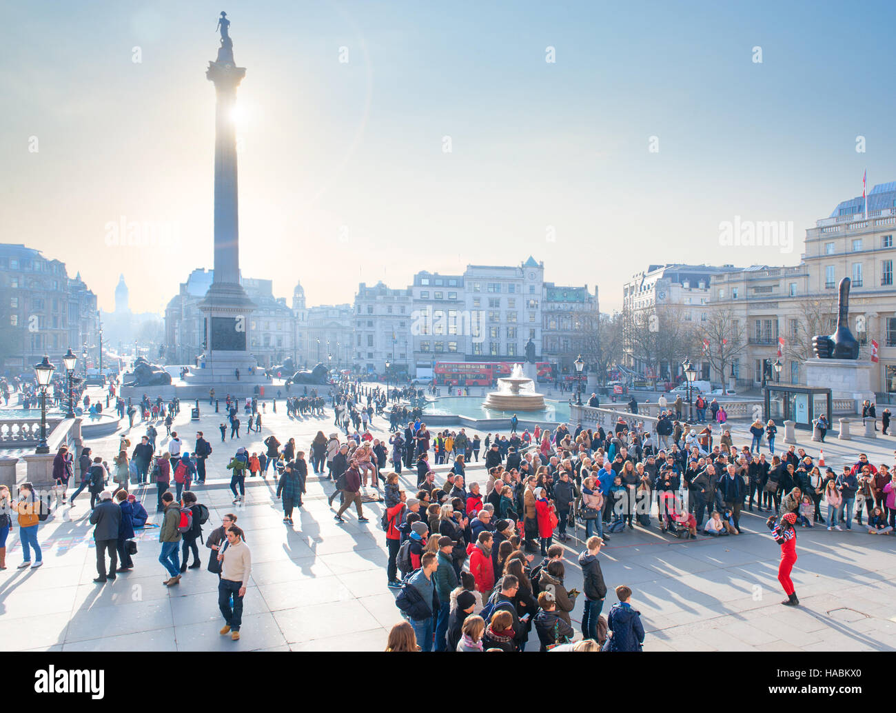 Les foules se rassemblent pour surveiller un artiste de rue à Trafalgar Square Londres avec l'hiver soleil derrière la colonne Nelson Banque D'Images