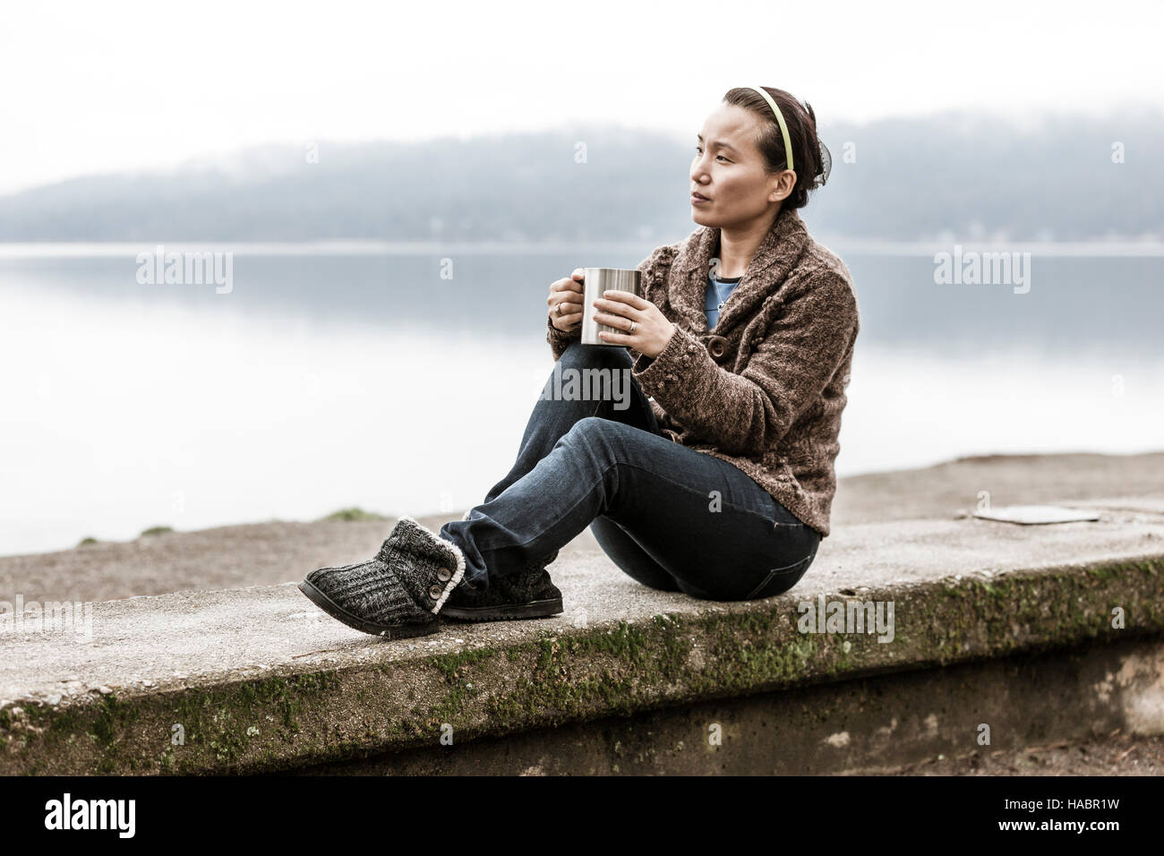 Femme assise sur vire par lac. Banque D'Images Femme assise sur vire par lac. Banque D'Images