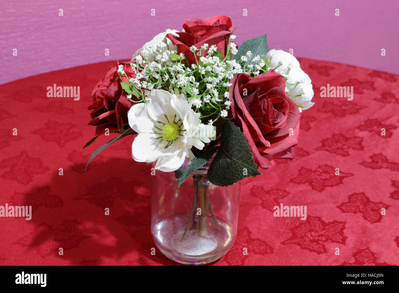 Fleurs en plastique décoratif dans un bocal en verre avec un chiffon de table rouge Banque D'Images