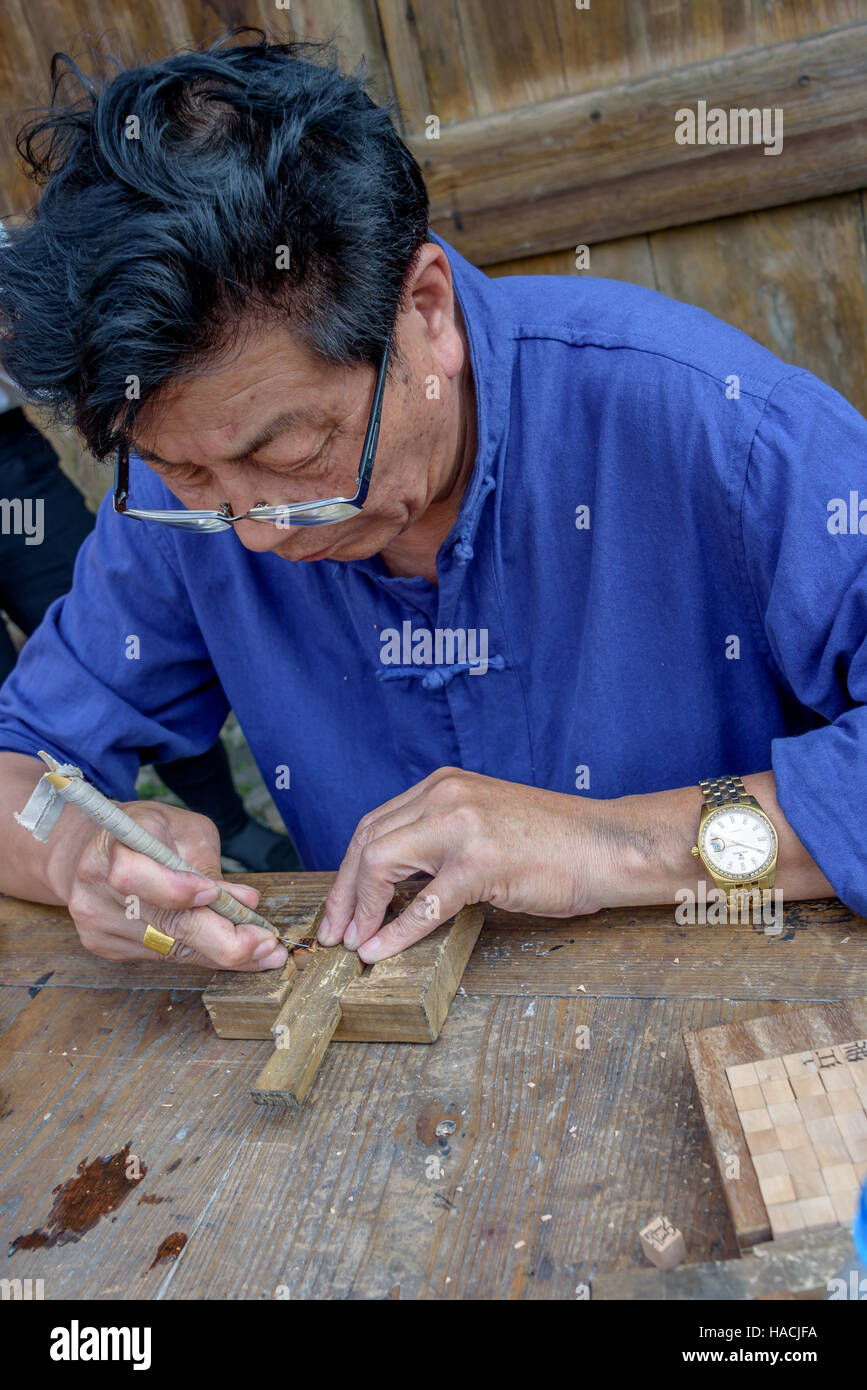 Un maître formé dans l'art chinois de l'impression à caractères mobiles en bois sculpte personnages au village Dongyuan, Huzhou, Chine. Banque D'Images