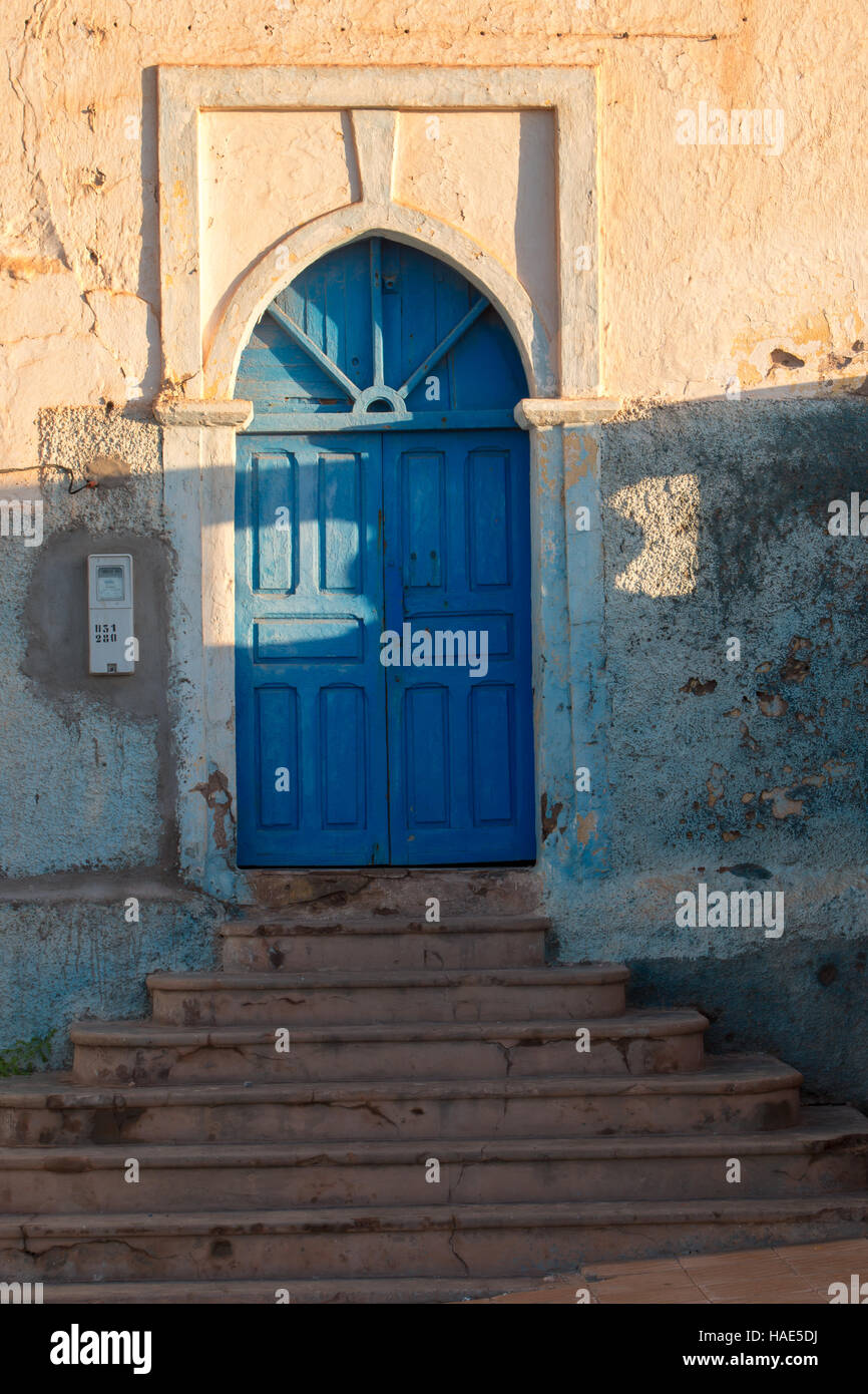 Entrée de la maison d'une rue escarpée. Plusieurs escaliers à la porte ouvragée bleu, éclairé par la lumière du soleil de fin d'après-midi. Sidi Ifni, Morocc Banque D'Images