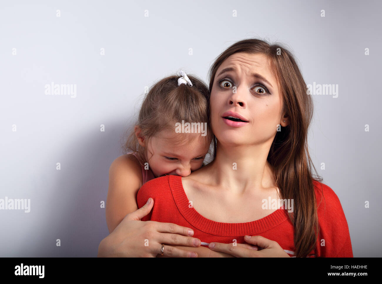 Angry Kid girl émotionnel vouloir mordre et son terroring choqué bagués effrayé mère avec de grands yeux sur fond bleu. Portrait concept Humour Banque D'Images