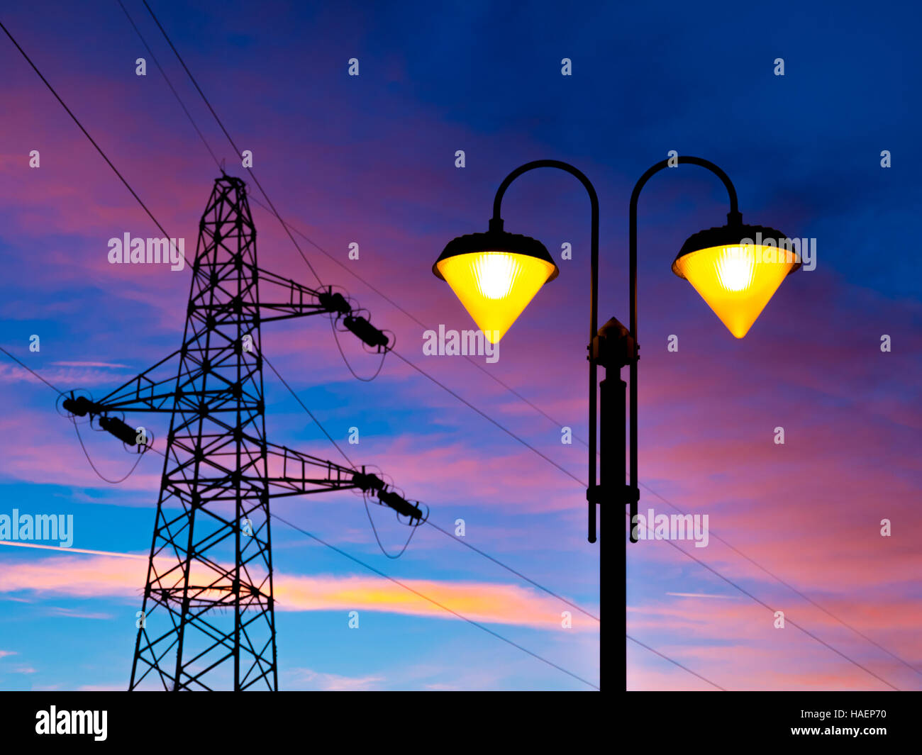 Allumée le réverbère au coucher du soleil avec la ligne haute tension et pylône sur l'arrière-plan Banque D'Images