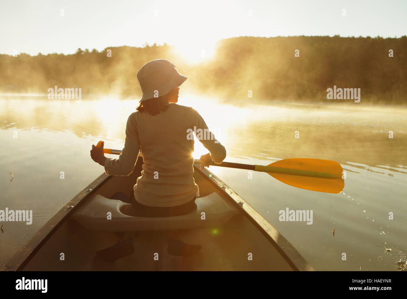 Jeune fille de canots sur un lac calme brumeux dans le Vermont en tant que le soleil se lève. Banque D'Images