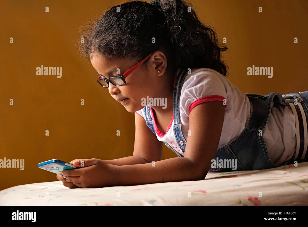 Petite fille à l'aide de mobile phone at home, Pune, Maharashtra. Banque D'Images