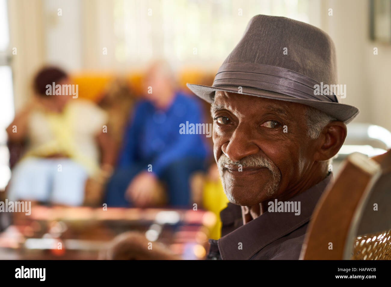 Portrait de personnes âgées black man looking at camera en maison de retraite, avec un groupe d'amis, en arrière-plan. Les patients en soins de détente pour les aînés. Banque D'Images