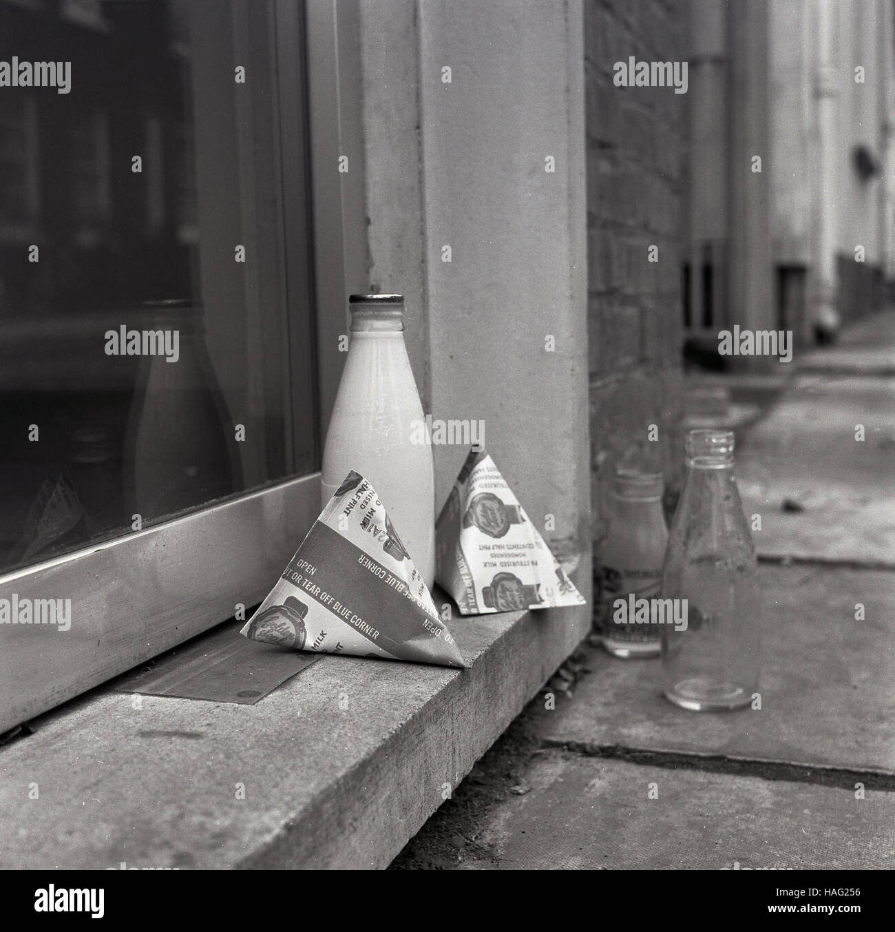 1965, historiques, une pinte de lait et bouteille de verre taille deux cartons de lait s'asseoir sur une maison porte, avec une bouteille de lait en verre vide debout sur la chaussée. Banque D'Images
