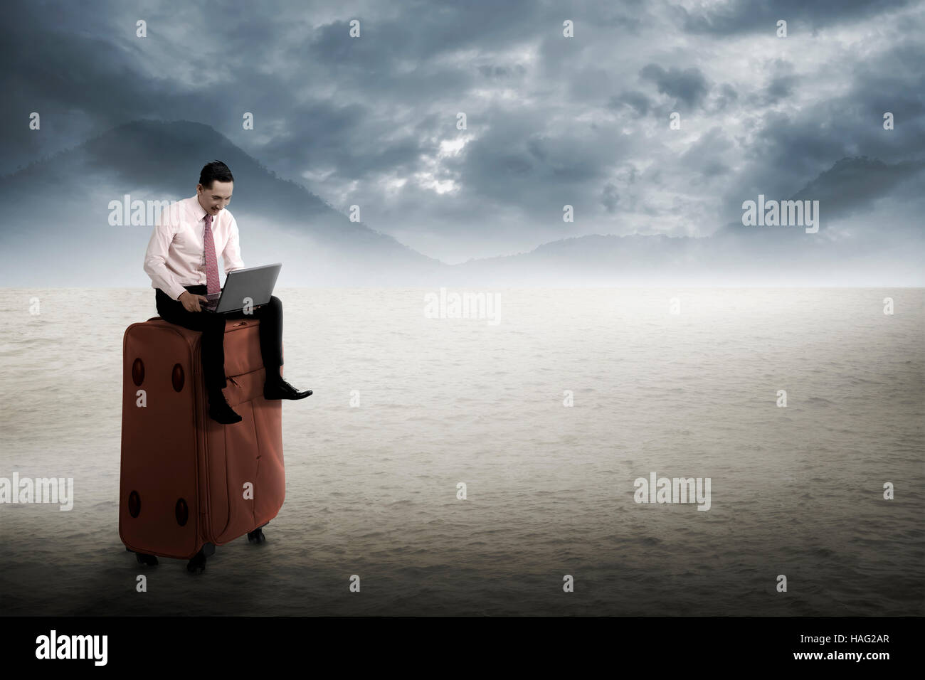 L'homme s'asseoir sur la valise, le travail avec ordinateur portable sur le désert. Concept de travail mobile Banque D'Images