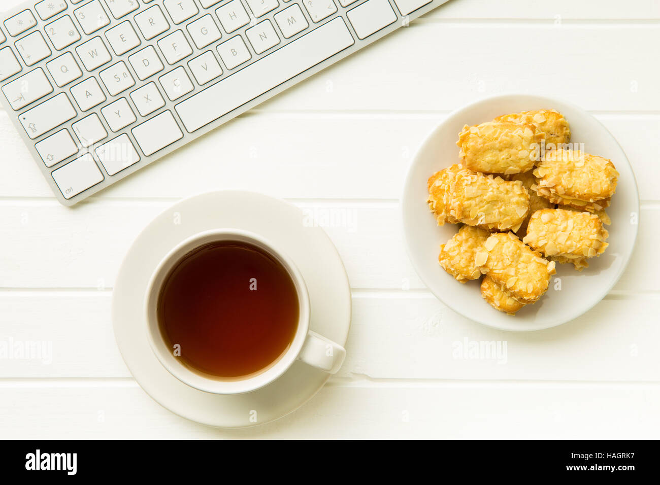 Pause pour le thé et biscuits aux amandes au bureau. Concept avec thé, biscuits et clavier de l'ordinateur. Banque D'Images