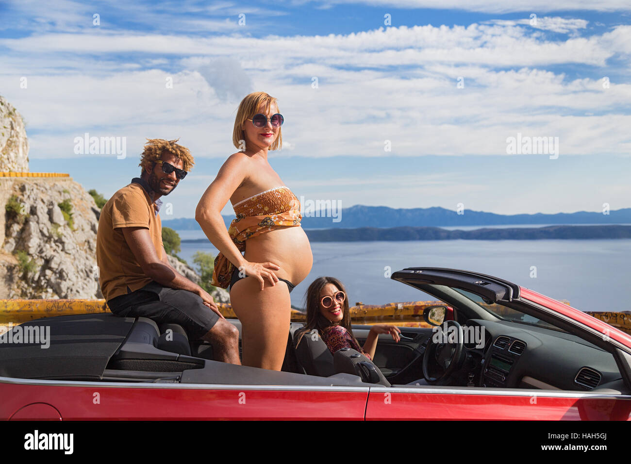 Groupe de jeunes heureux dans la red convertible. femme enceinte montrant son ventre. Banque D'Images