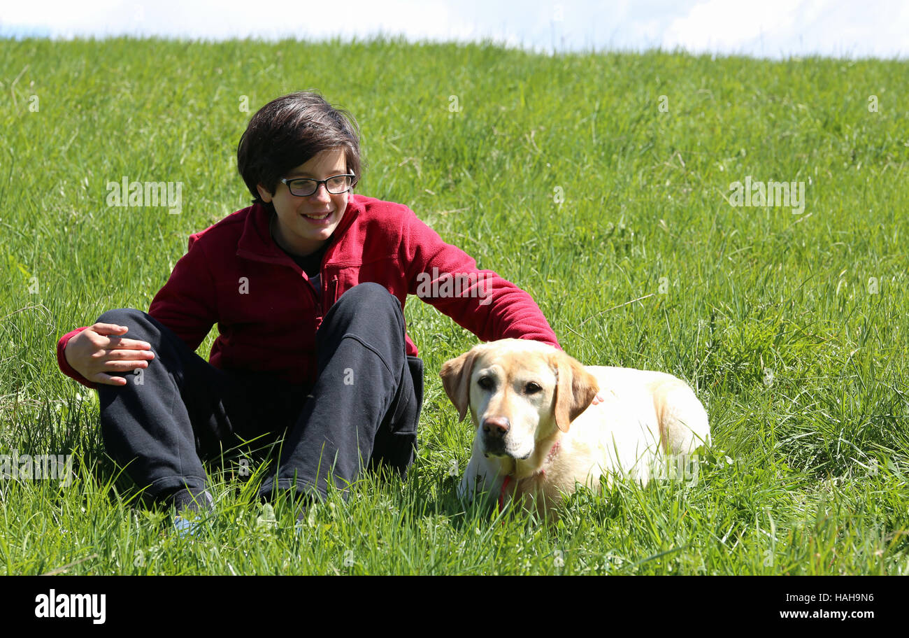 Smiling boy sur le pré dans la montagne avec son chien Labrador Retriever jaune Banque D'Images