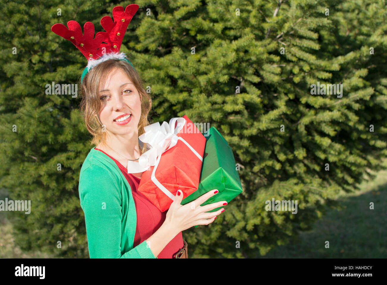 Belle fille avec des oreilles de renne holding présente en face de grand sapin Banque D'Images