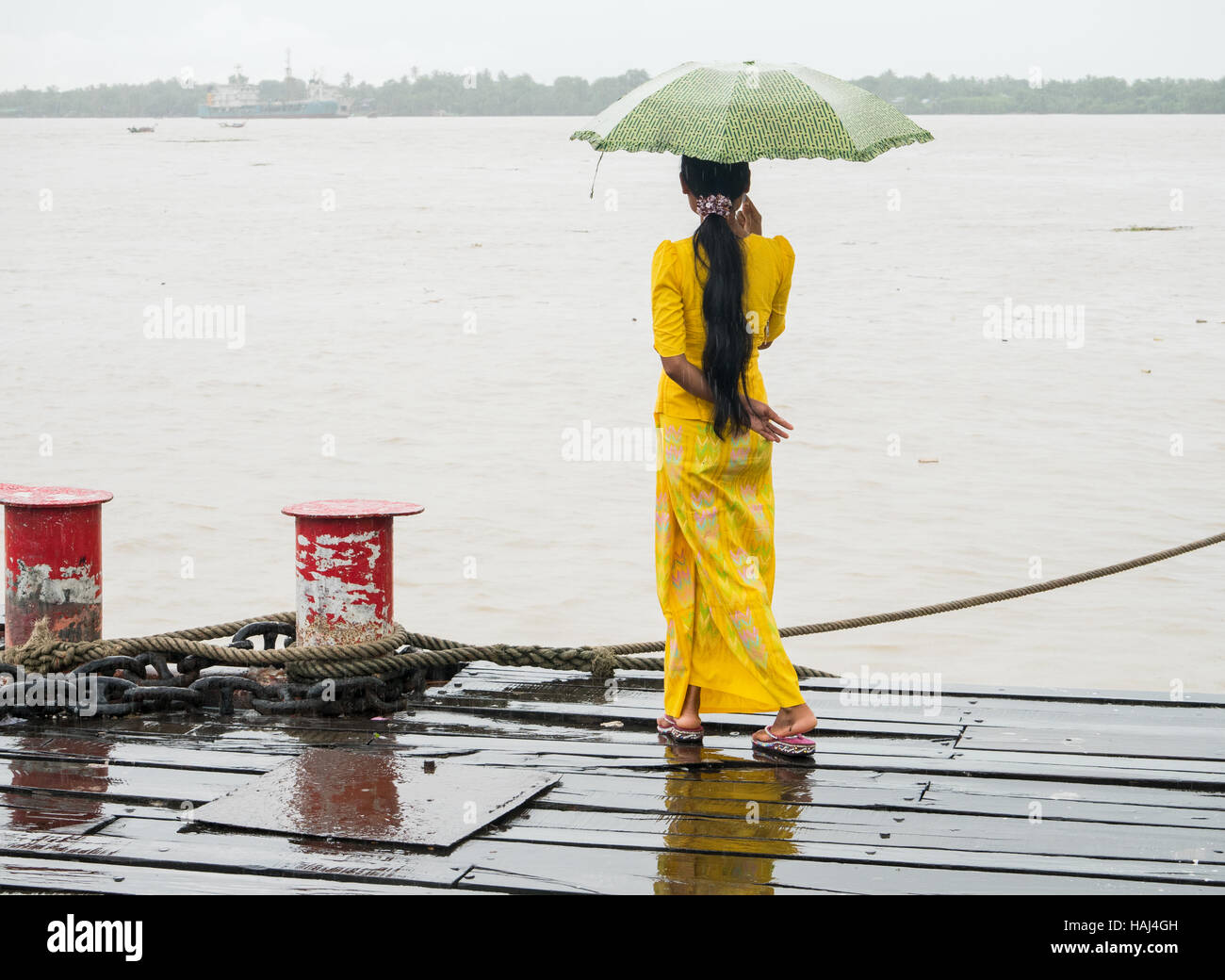 Jeune femme birmane en vêtements traditionnels en regardant le fleuve Yangon à partir de la jetée de Botahtaung un jour de pluie. Banque D'Images