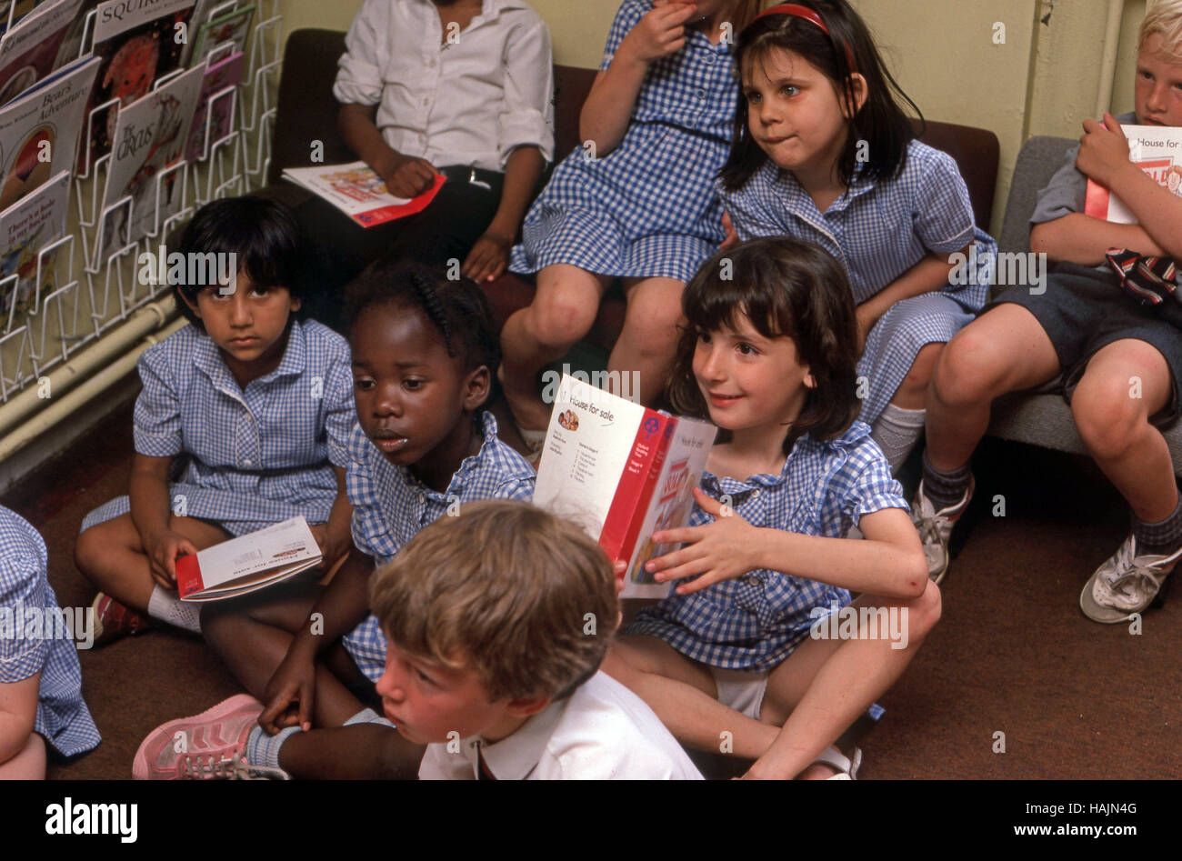 Les enfants de l'école primaire sur le plancher dans un coin lecture avec des livres Banque D'Images