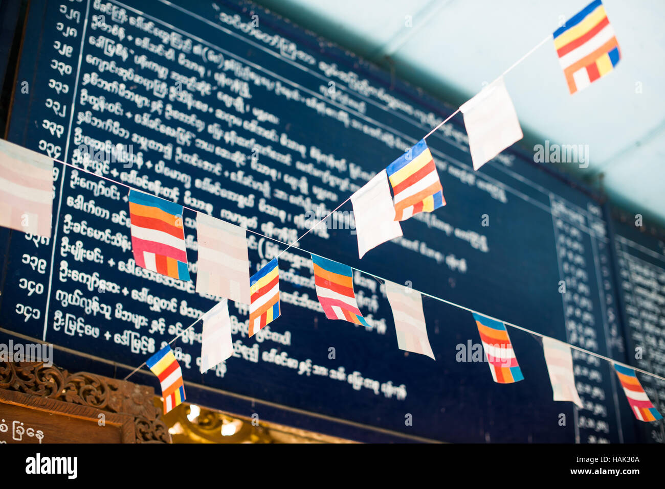 Drapeaux du temple Manuha Bagan Myanmar // BAGAN, Myanmar — drapeaux et reconnaissance des donateurs exposés au temple Manuha, l'un des monuments bouddhistes les plus importants de Bagan au XIe siècle. Construit en 1067 EC par le roi mon Manuha après sa défaite par le roi Anawrahta du Royaume païen, le temple abrite quatre images monumentales de Bouddha délibérément positionnées dans des chambres exiguës pour symboliser la détresse psychologique du roi emprisonné. Le temple est réputé pour ses trois statues de Bouddha assises et son immense Bouddha couché, avec les espaces intérieurs restreints représentant la frustration de Manuha pendant Banque D'Images