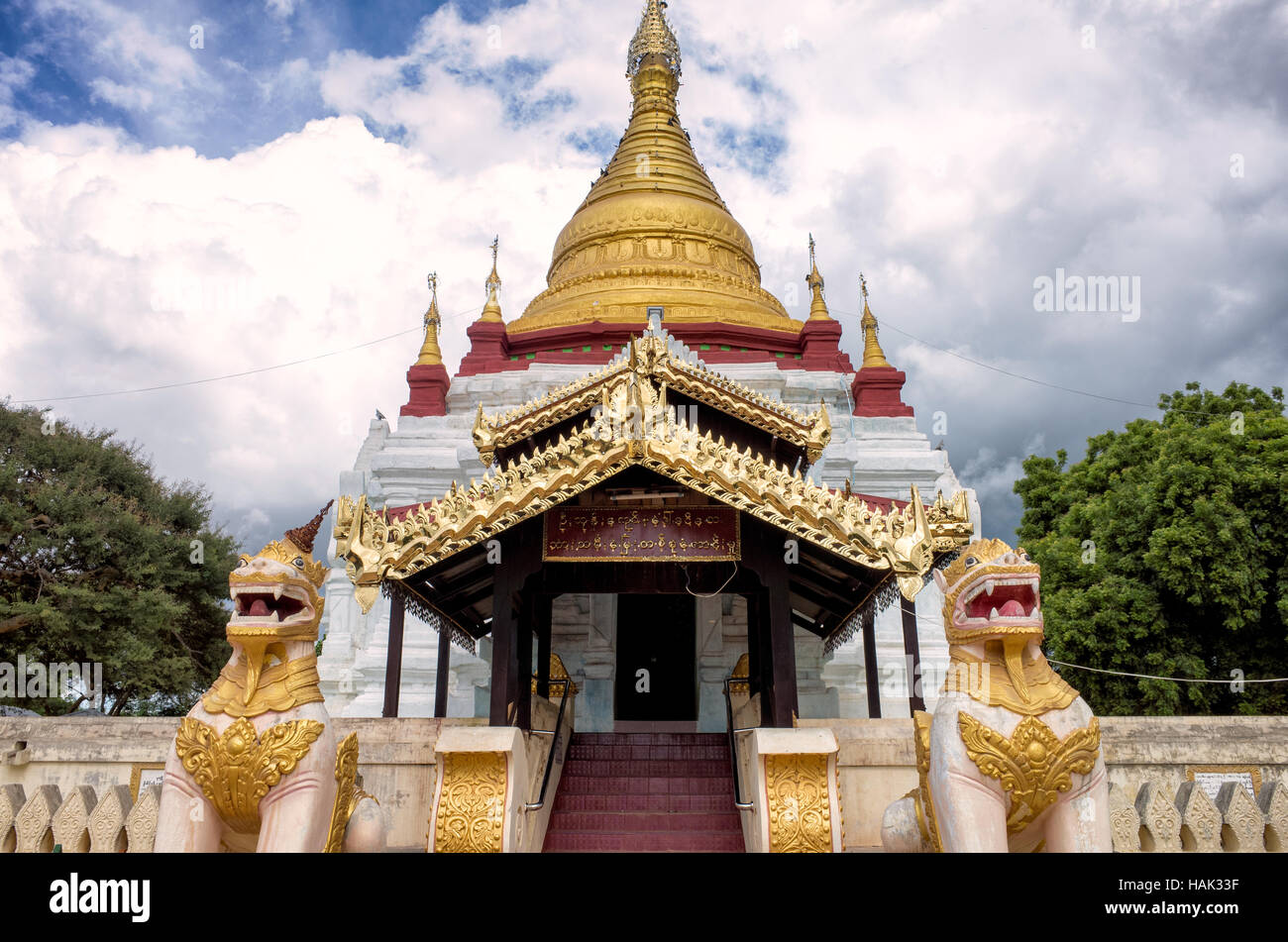 Temple Shwe Kyaung U Lions gardiens Bagan Myanmar // BAGAN, Myanmar — L'entrée principale du temple Shwe Kyaung U, flanquée de deux statues de lion gardien qui protègent traditionnellement les espaces sacrés bouddhistes des influences négatives. Ce temple du XVIIIe siècle est situé dans un monastère du village de Taungbi dans le vieux Bagan, représentant l'architecture religieuse à plus petite échelle qui servait les communautés monastiques locales pendant la période Konbaung. Le temple présente un pavillon en bois distinctif ajouté sur sa face ouest, démontrant comment l'architecture traditionnelle du temple en briques a été adaptée pour rencontrer th Banque D'Images