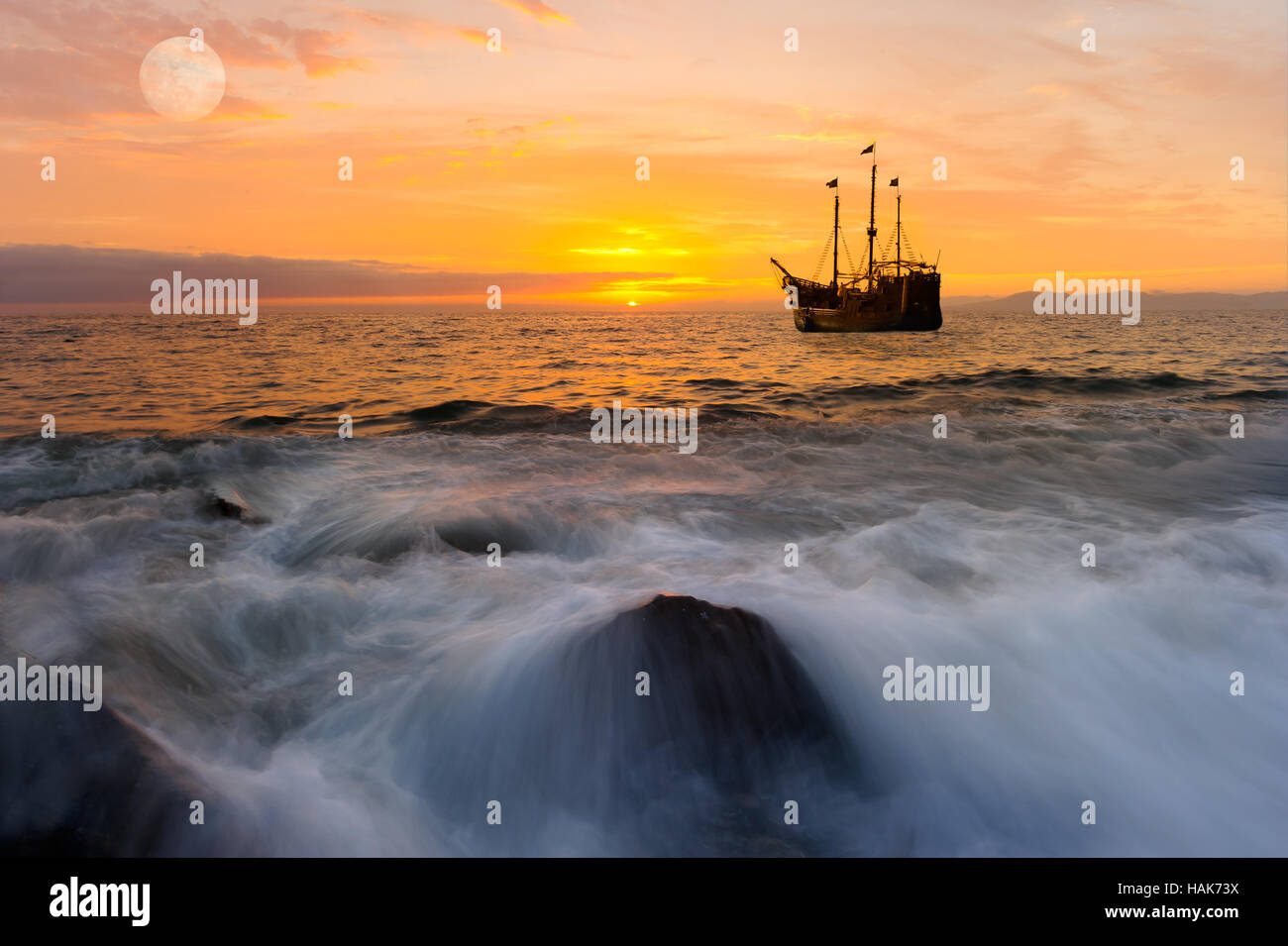 Ocean sunset ship est un ancien bateau de pirate en mer avec drapeaux flottants au coucher du soleil dans un ciel rempli de couleur orange. Banque D'Images