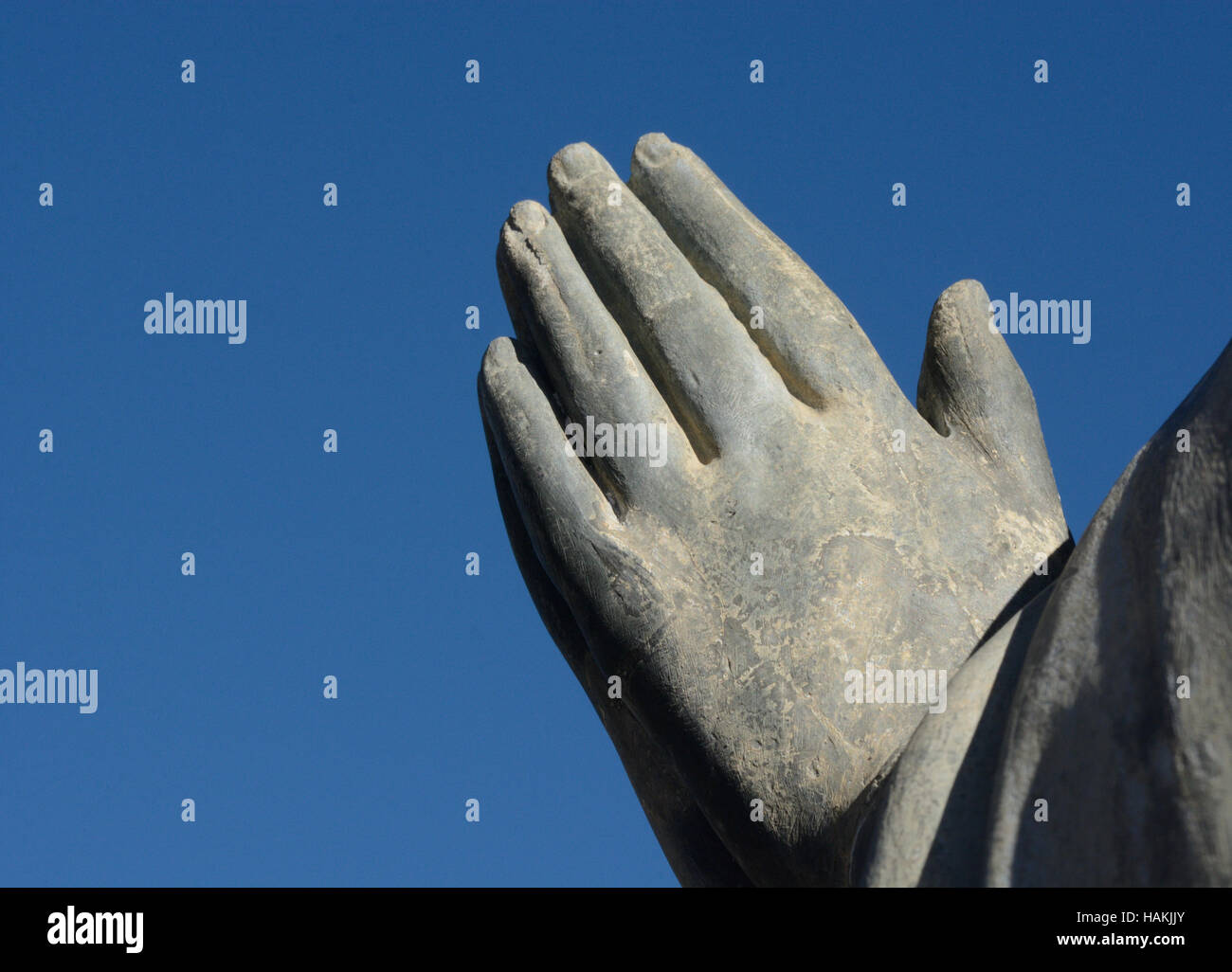Les mains de pierre dans la prière contre le ciel bleu Banque D'Images