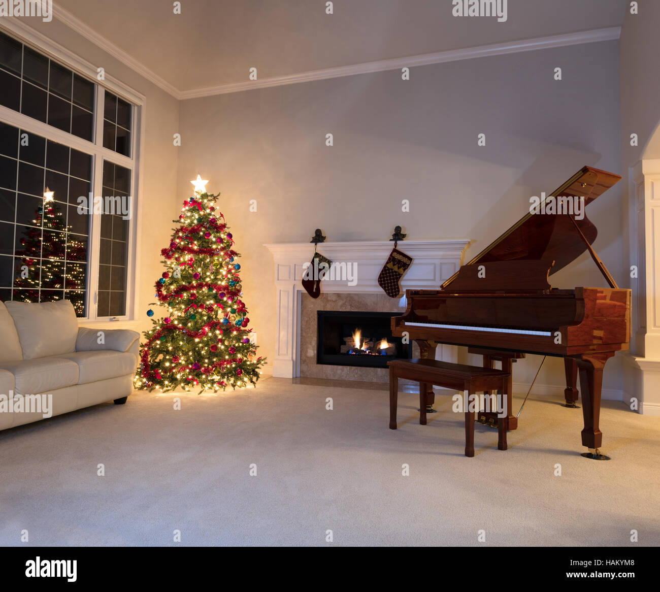 Arbre de Noël lumineux dans la salle de séjour avec cheminée et piano pendant la nuit. Banque D'Images