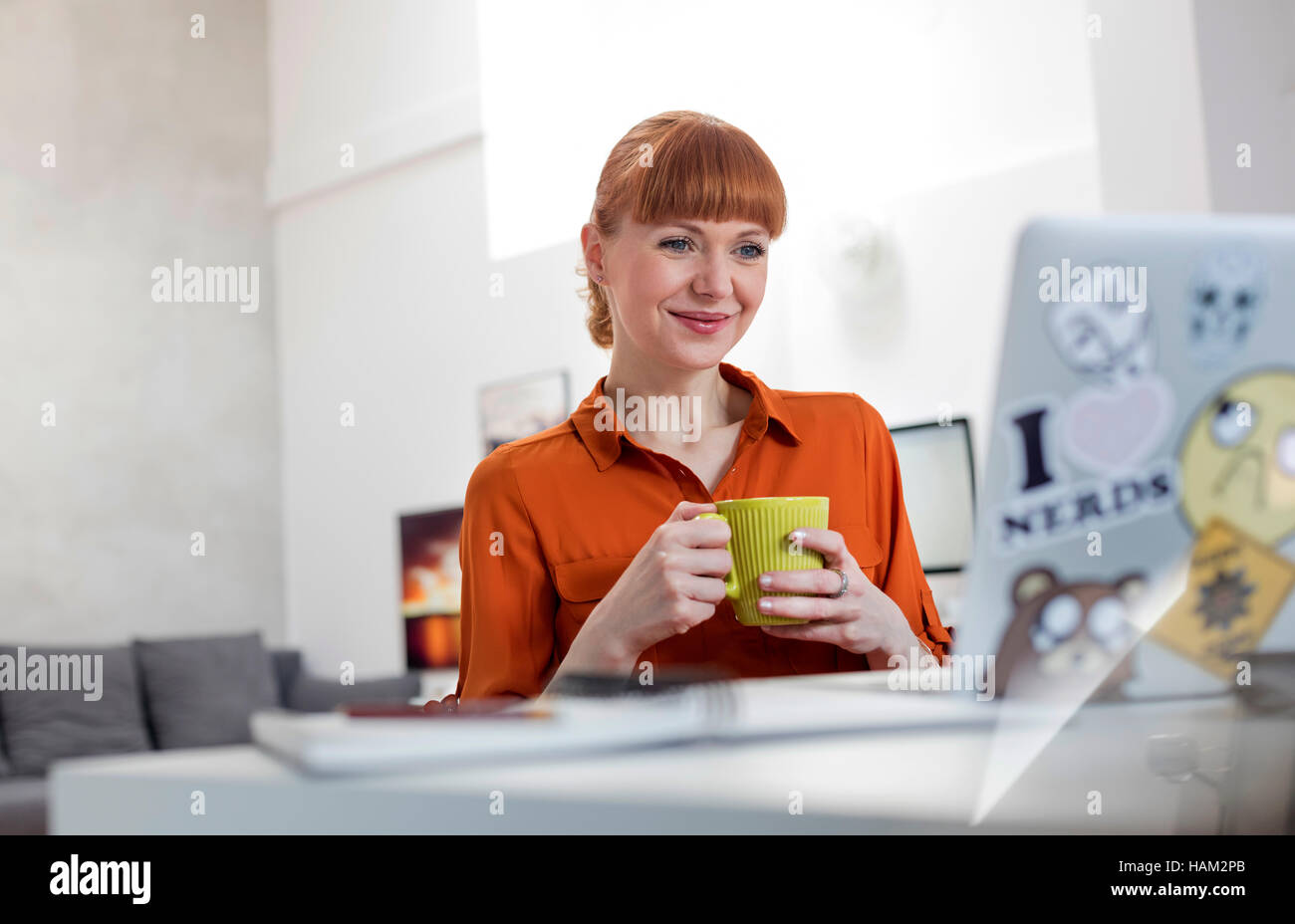 Smiling woman drinking coffee and working at laptop Banque D'Images