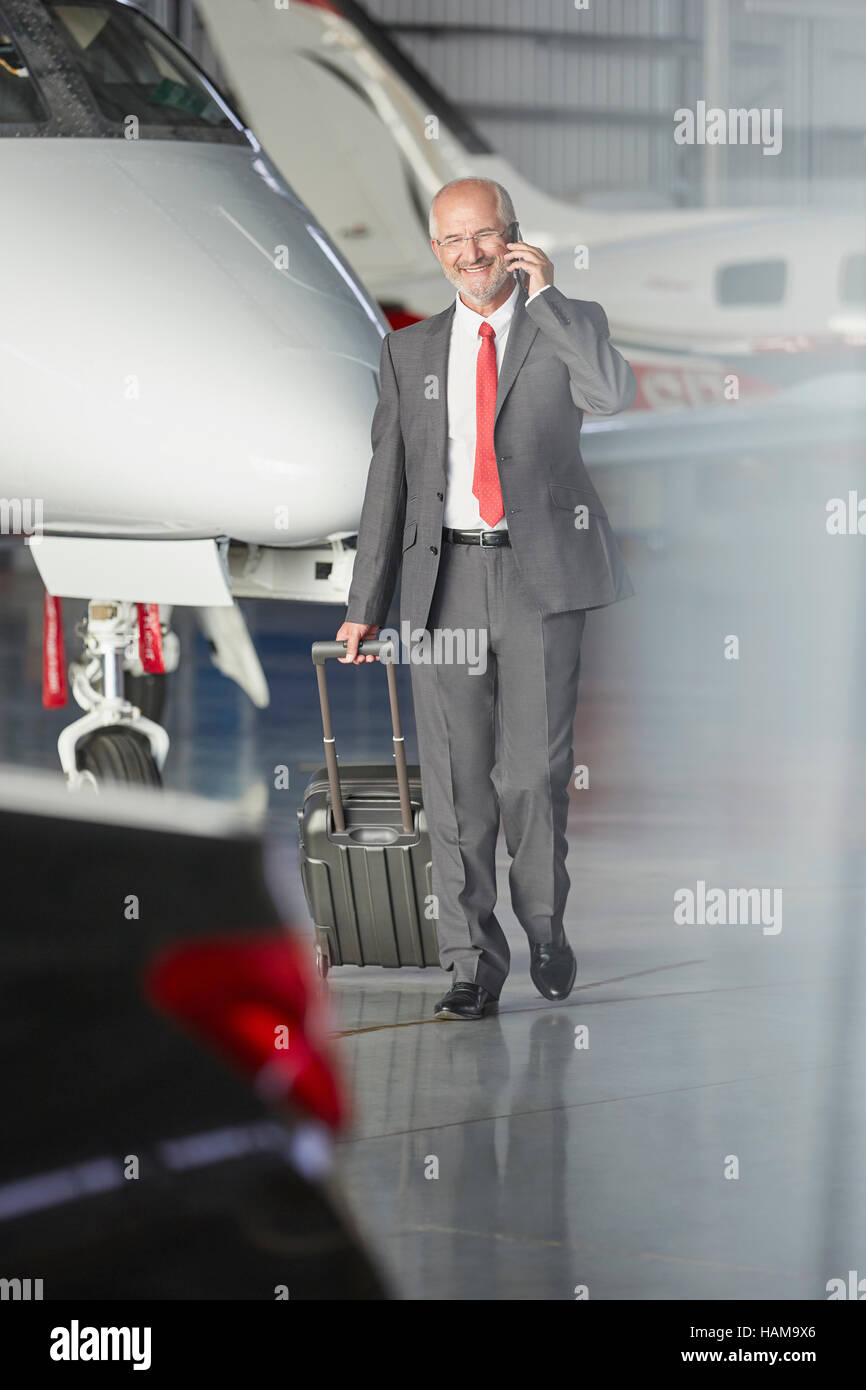 Smiling businessman pulling suitcase in airplane hangar Banque D'Images