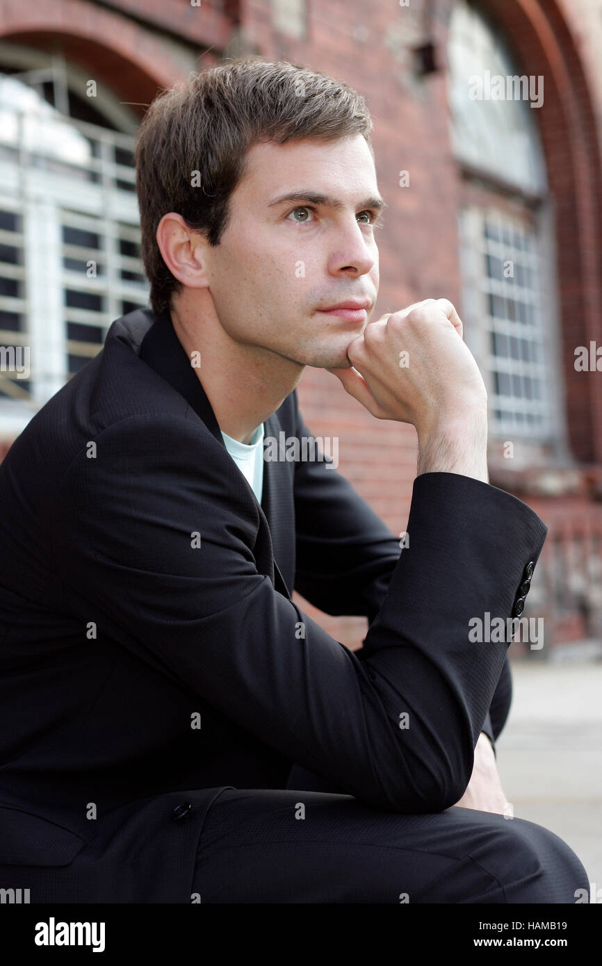 Portrait d'un jeune homme portant un costume, assis en face d'un bâtiment industriel fait de briques rouges et de penser Banque D'Images