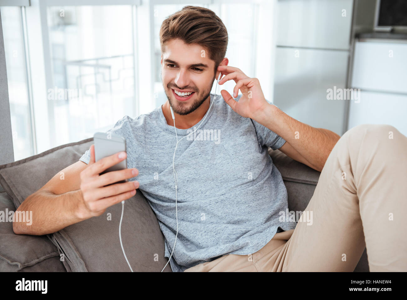 Homme heureux des écouteurs pour écouter de la musique tout en se trouve sur le canapé. À la recherche sur le téléphone et la messagerie. Banque D'Images