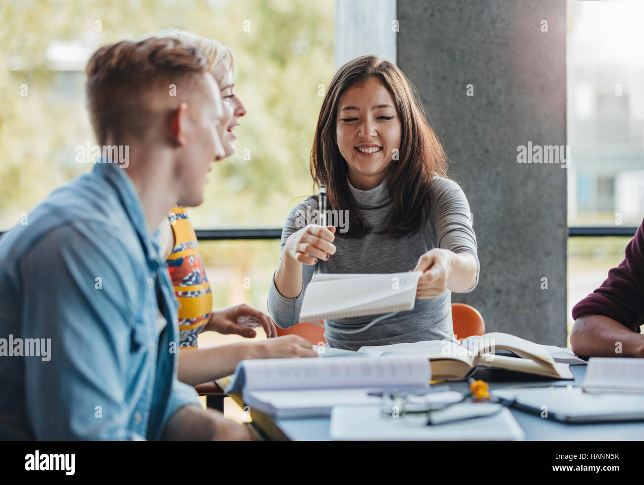 Les jeunes gens assis à table partage de notes pour le travail scolaire. Groupe d'étudiants d'étudier ensemble dans une bibliothèque. Banque D'Images