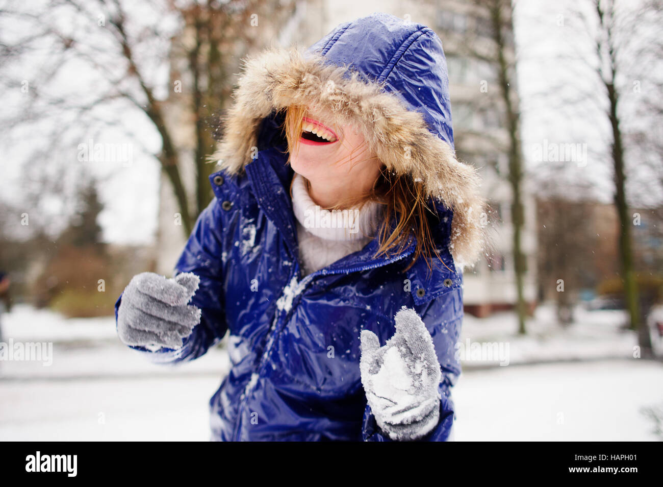 Jeune femme rire après lutte par des boules de neige. Le visage de la femme  est à moitié caché par une capuche. Un manteau et des gants dans la neige,  les cheveux