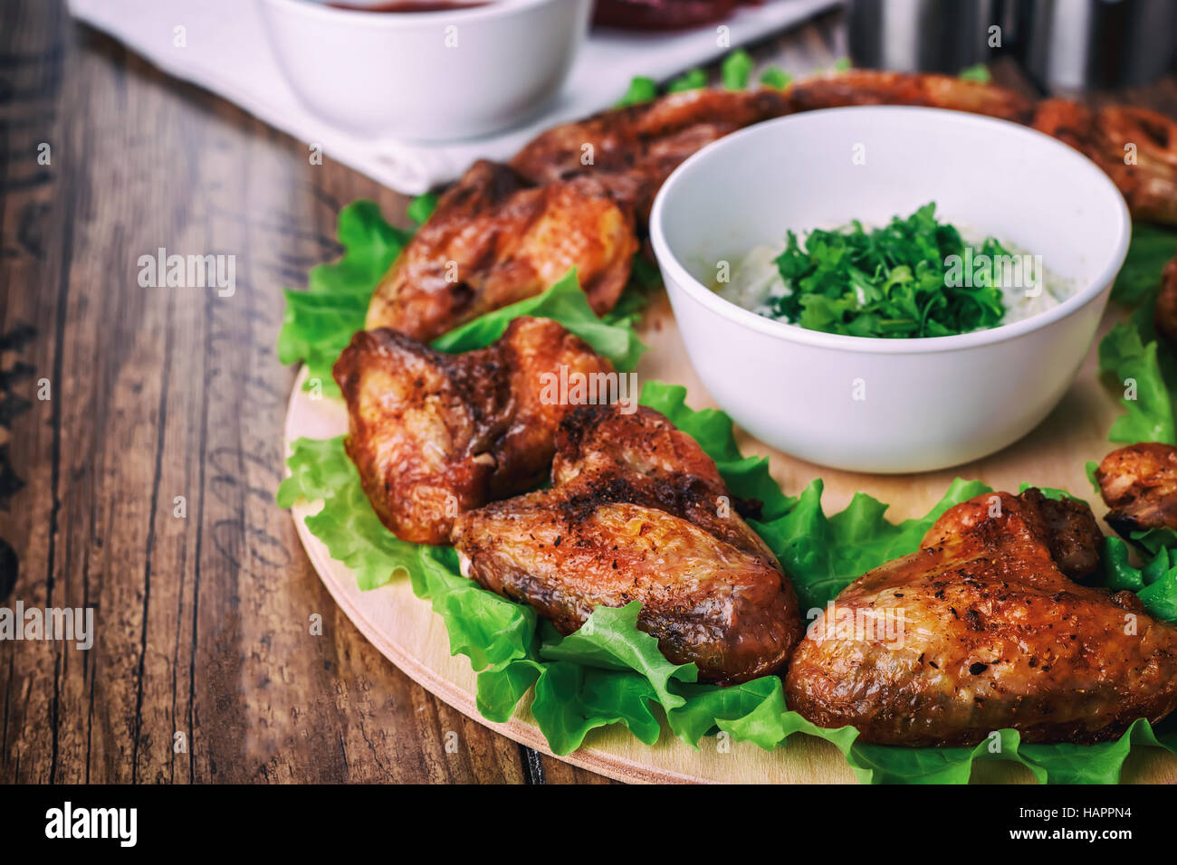Ailes de poulet délicieux grillés à l'ail et de la sauce tomate avec de la laitue sur une carte ronde sur fond rustique en bois Banque D'Images