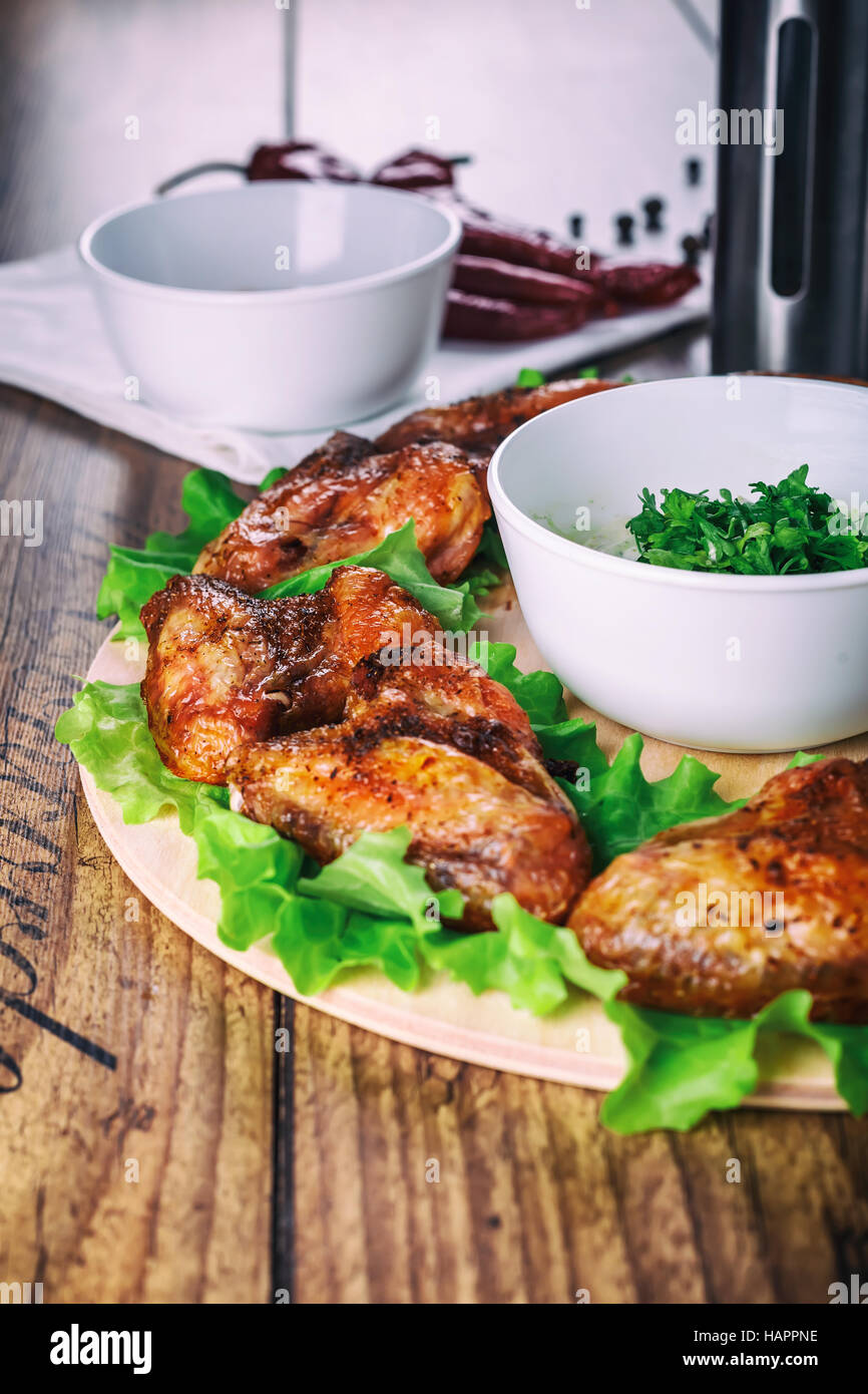 Ailes de poulet délicieux grillés à l'ail et de la sauce tomate avec de la laitue sur une carte ronde sur fond rustique en bois Banque D'Images