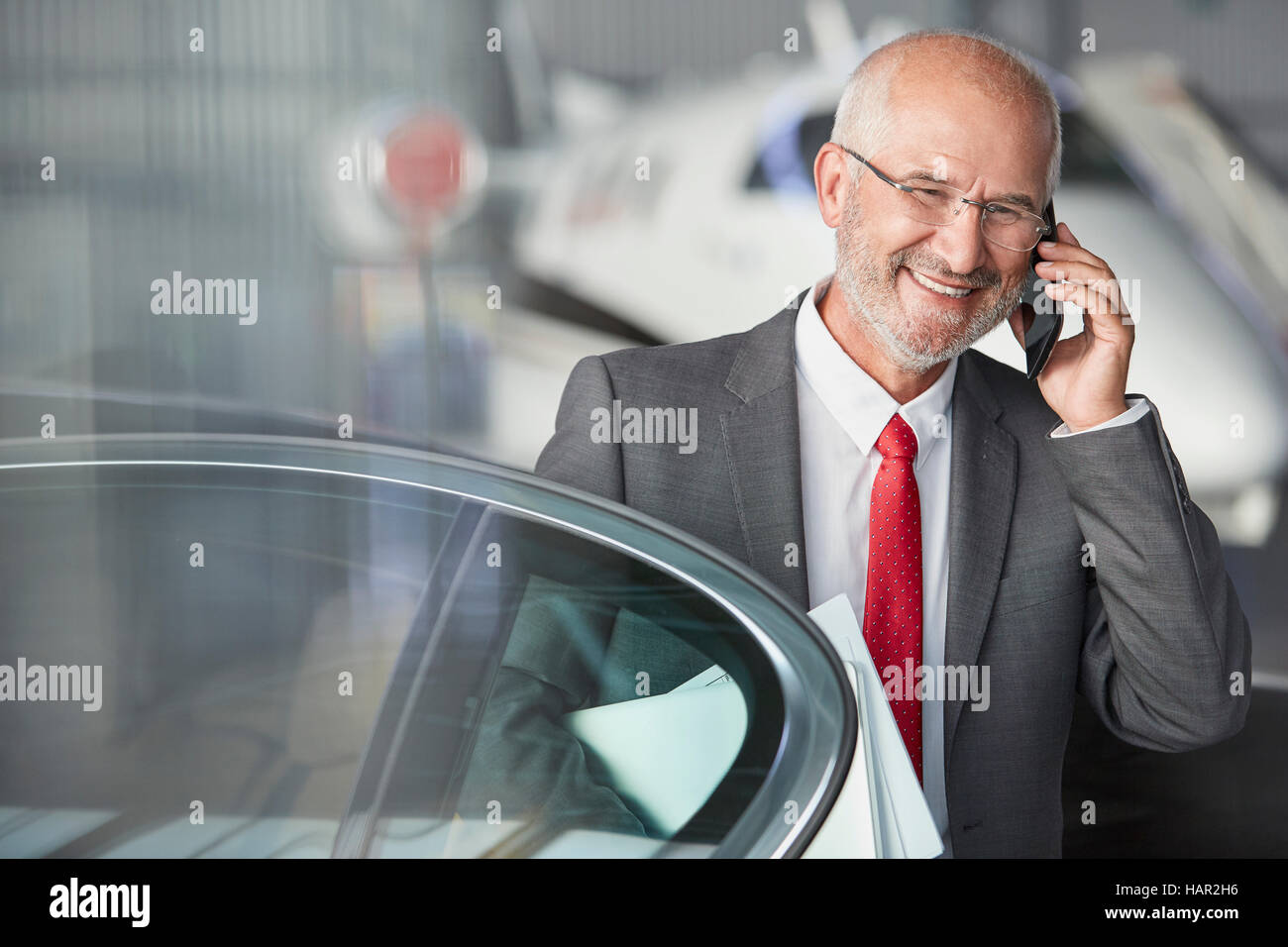 Smiling businessman talking on cell phone in airplane hangar Banque D'Images