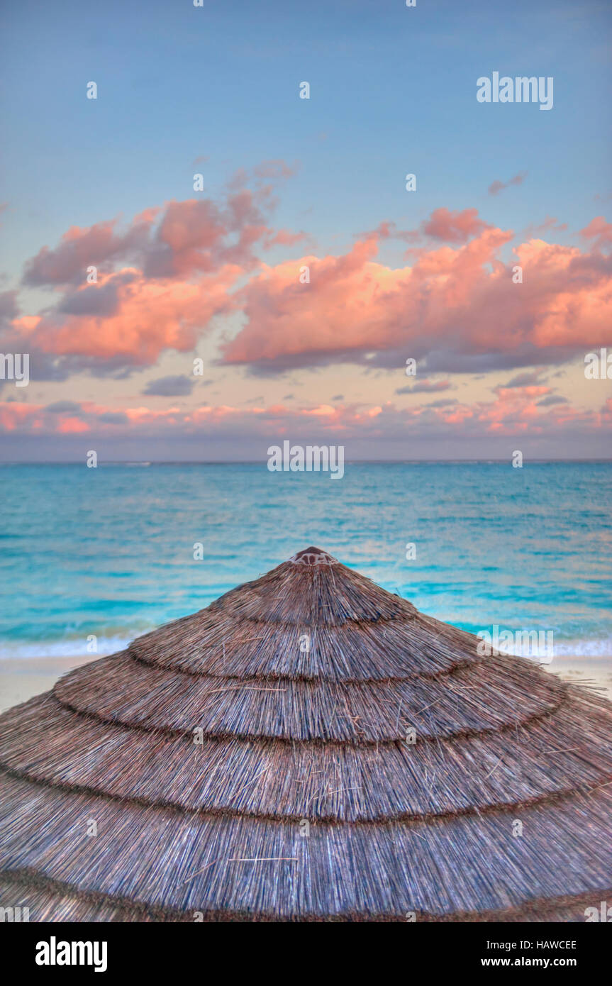 Lever de soleil sur la plage de l'île des Caraïbes des Îles Turques-et-Caïques. Un toit de chaume resort est situé au large de la mer turquoise / bleu avec des vagues de sable et les nuages roses Banque D'Images