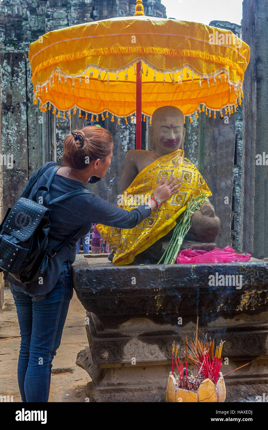 Une jeune femme met sa main sur le coeur de Bouddha à un culte dans l'ancien temple du complexe d'Angkor Thom. Banque D'Images