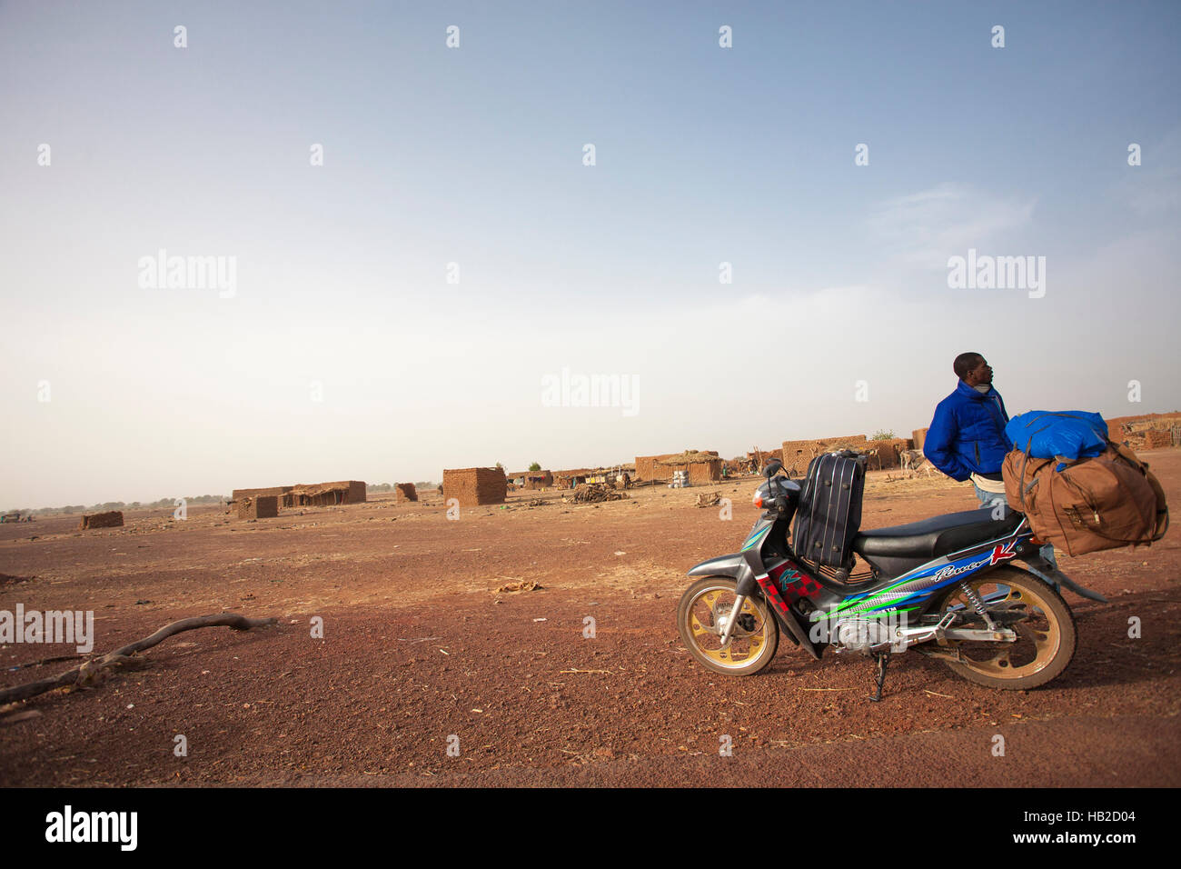 MOPTI, MALI - 1 janvier : Jeune homme migrants d'Afrique noire en attente devant son scooter chargé avec des bagages dans la campagne de Mopti Banque D'Images