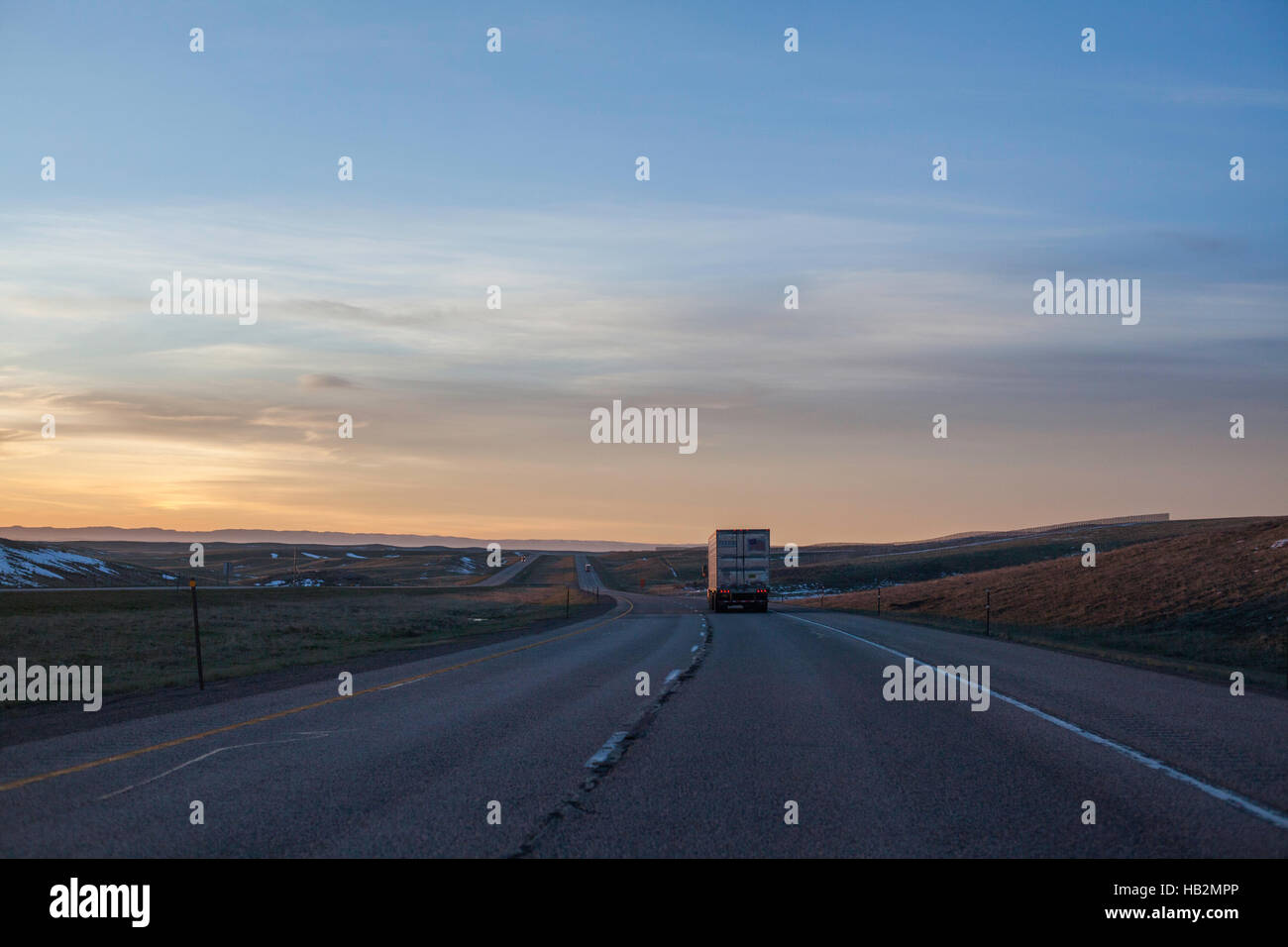 L'autoroute vers un lever du soleil avec un camion dans l'avant-plan sur une route sinueuse. Banque D'Images