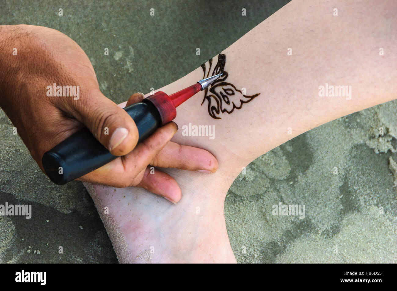 Part d'un artiste en peinture d'un motif papillon à la cheville d'un client à l'aide de colorant au henné. Banque D'Images