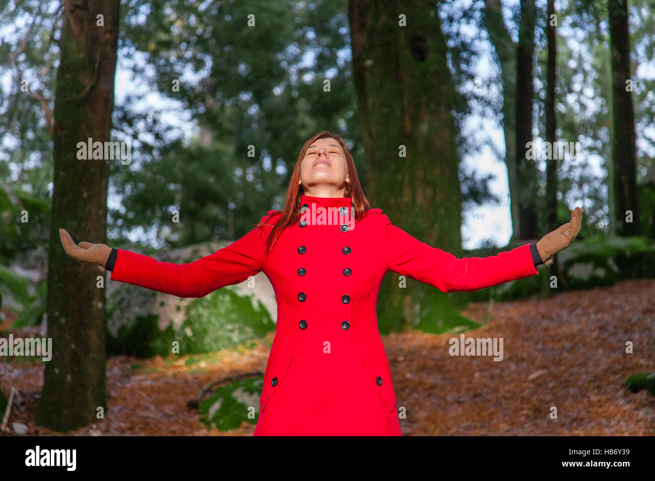 Femme jouissant de la chaleur du soleil d'hiver sur une forêt portant un long manteau rouge Banque D'Images