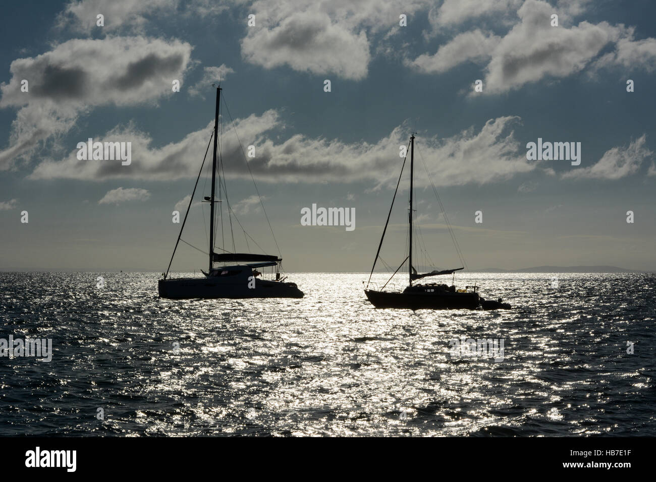 Deux yachts ancrés dans la baie de Tenby tôt un matin d'été. Ciel bleu avec des nuages blancs moelleux et le soleil reflétant sur la mer. Banque D'Images