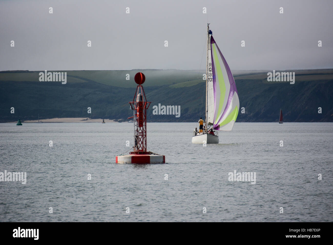 Classic yacht de croisière avec approche de la chute Le Qatar bouée dans Milford Haven, avec Watwick beach dans l'arrière-plan Banque D'Images