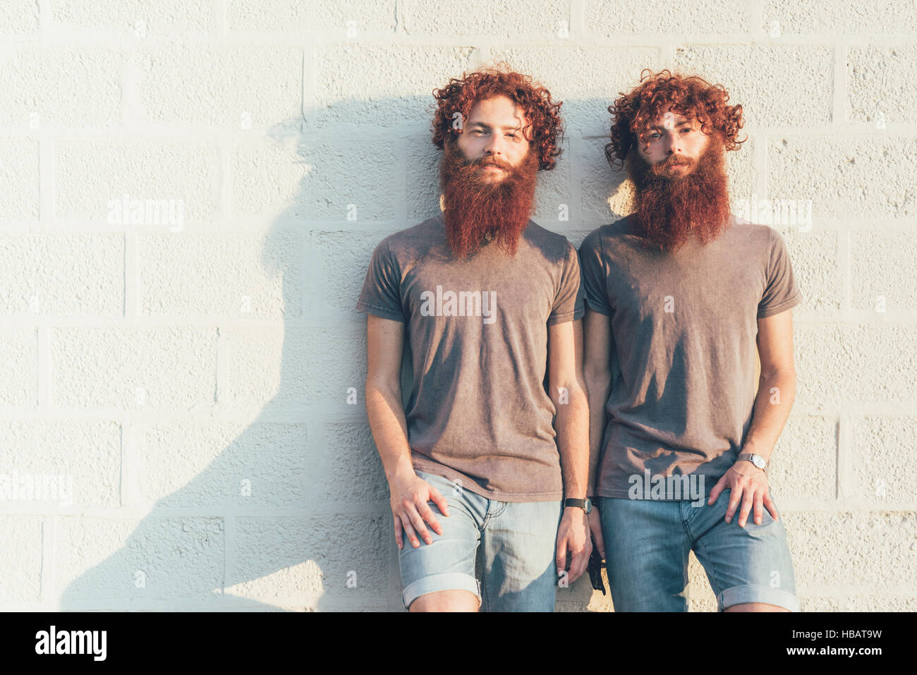 Portrait de jumeaux mâles adultes identiques aux cheveux rouges et barbes contre mur Banque D'Images